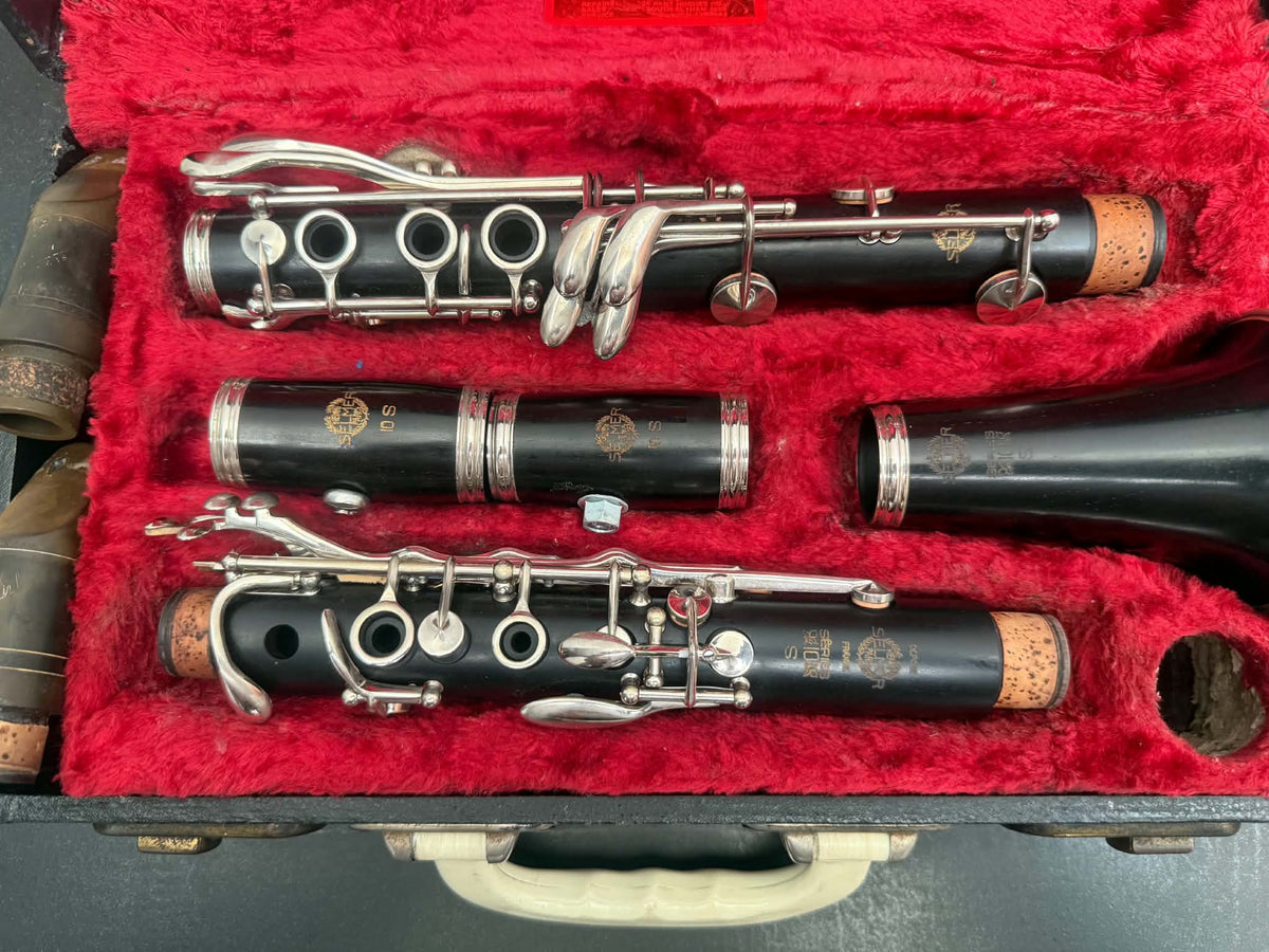 A black wood clarinet set displayed inside an open case lined with bright red velvet. The set includes the clarinet body, mouthpiece, barrel, and right handpiece with silver-tone metal keys and valves.